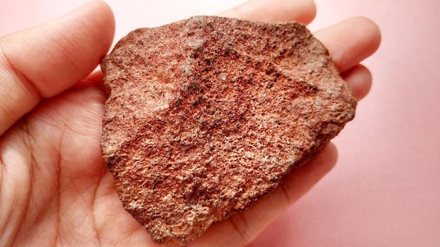 Close-up of a handful of raw copper ore freshly mined from a Peruvian copper mine, showing the metallic sheen and texture of the ore with a blurred background of mining equipment.
