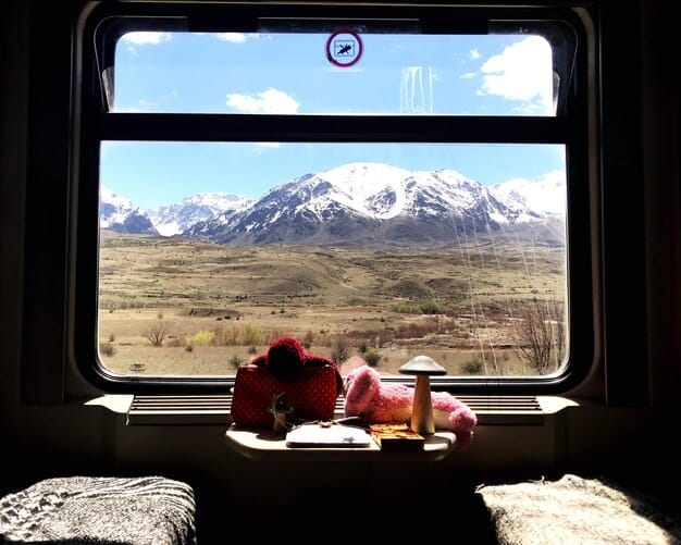 Interior of a plush, luxurious train car with large windows showing the Andean landscape passing by. Passengers are seated comfortably, enjoying drinks and conversation.
