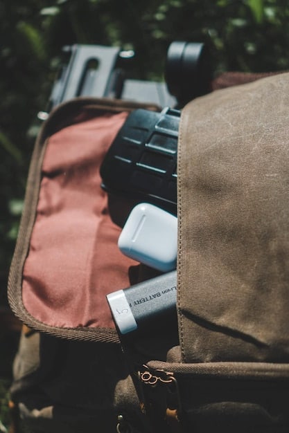 A close-up shot of essential gear for a wildlife spotting trip in the Amazon. The image includes a pair of binoculars, a lightweight long-sleeved shirt, a bottle of insect repellent, sunscreen, a hat, and a waterproof bag. Arrange the items neatly on a wooden surface with a jungle background to convey the context.