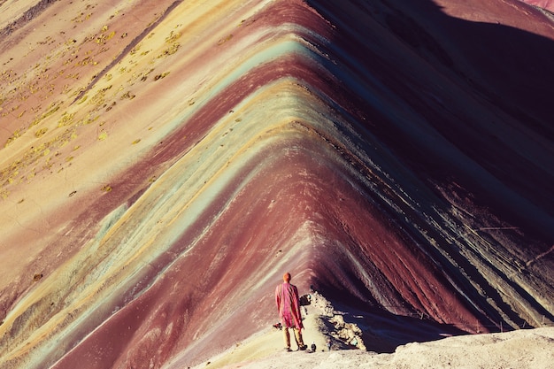 A close-up shot of the colorful striations on Rainbow Mountain, showing the distinct layers of red, yellow, green, and brown minerals. The sunlight catches the textures of the rock, highlighting the natural beauty and geological processes that created this unique landscape. The image focuses on the details of the mountain's surface, rather than the overall vista.