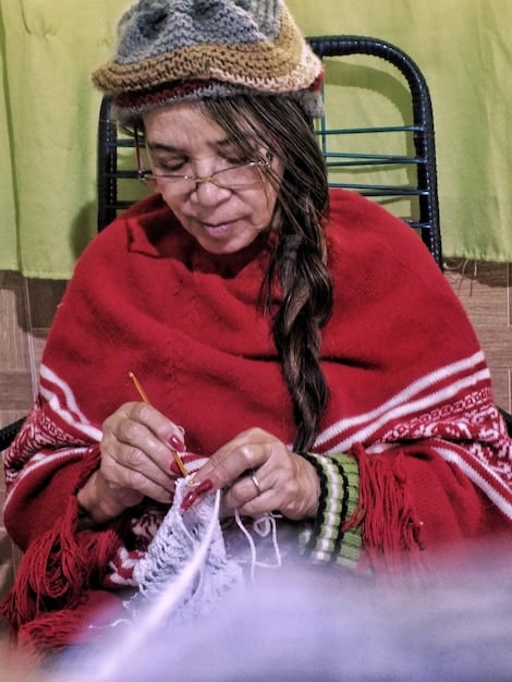 A photo of a local Andean woman in traditional clothing, smiling and selling handmade textiles near Rainbow Mountain. The vibrant colors of her clothing and the textiles contrast with the natural colors of the mountain in the background. The image showcases the local culture and the economic activities that support the community.