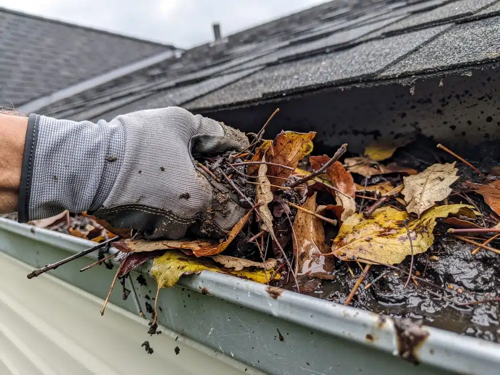 Hand cleaning clogged gutter on a house